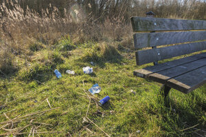 Trash littered on the ground near a park bench in a natural sett