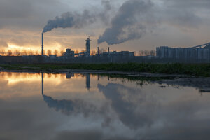 Industriecomplex bij zonsondergang, weerspiegeld in plas