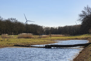 Wind turbines stand tall beside a tranquil river surrounded by t