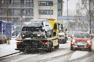 Takelwagen vervoert beschadigde auto in besneeuwde stad