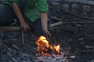 Persoon steekt vuur aan met takjes bij schemering