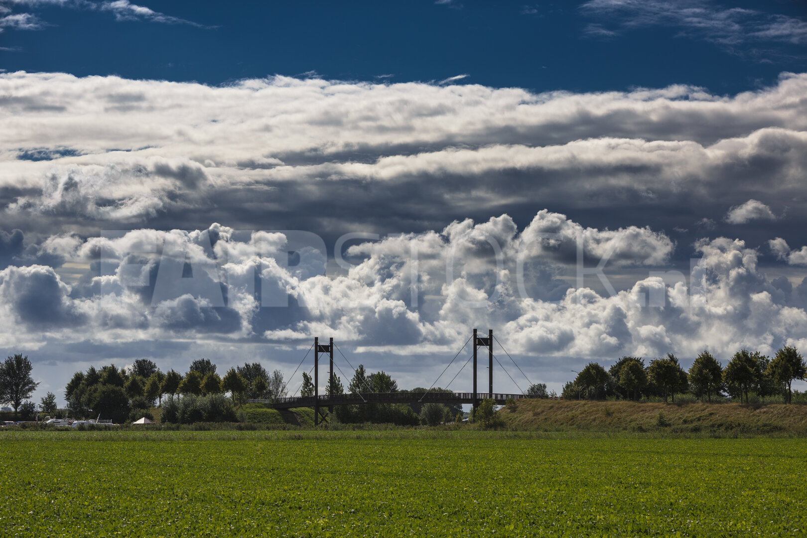 Wolken boven groen veld met brug in de verte