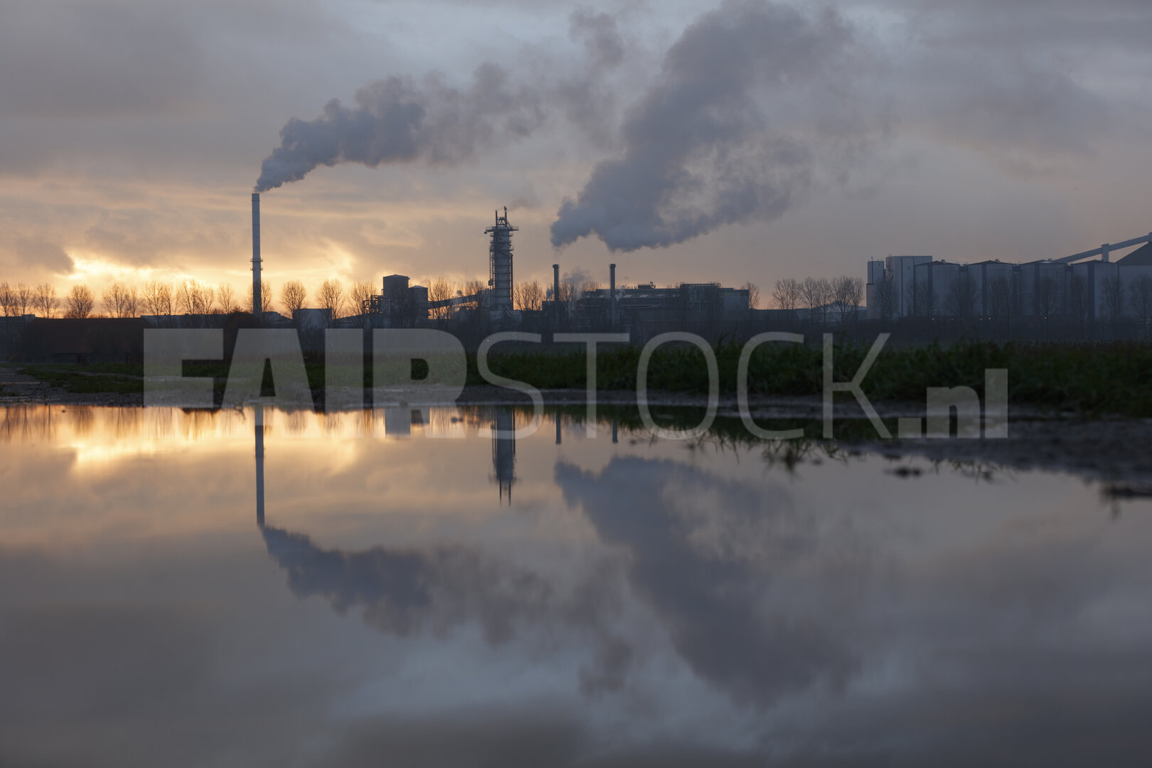 Industrieel complex bij schemering, weerspiegeld in plas