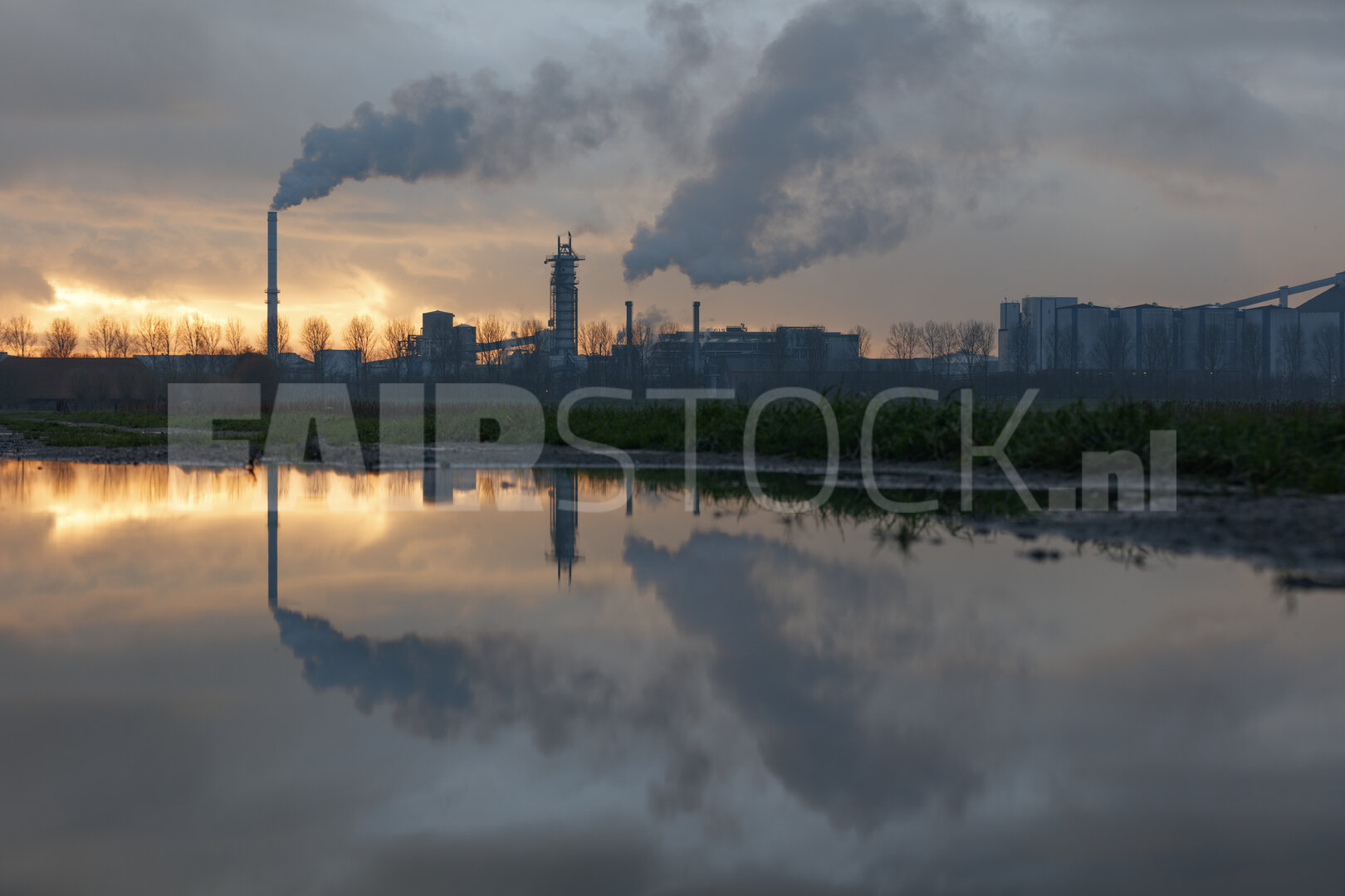 Industriecomplex bij zonsondergang, weerspiegeld in plas