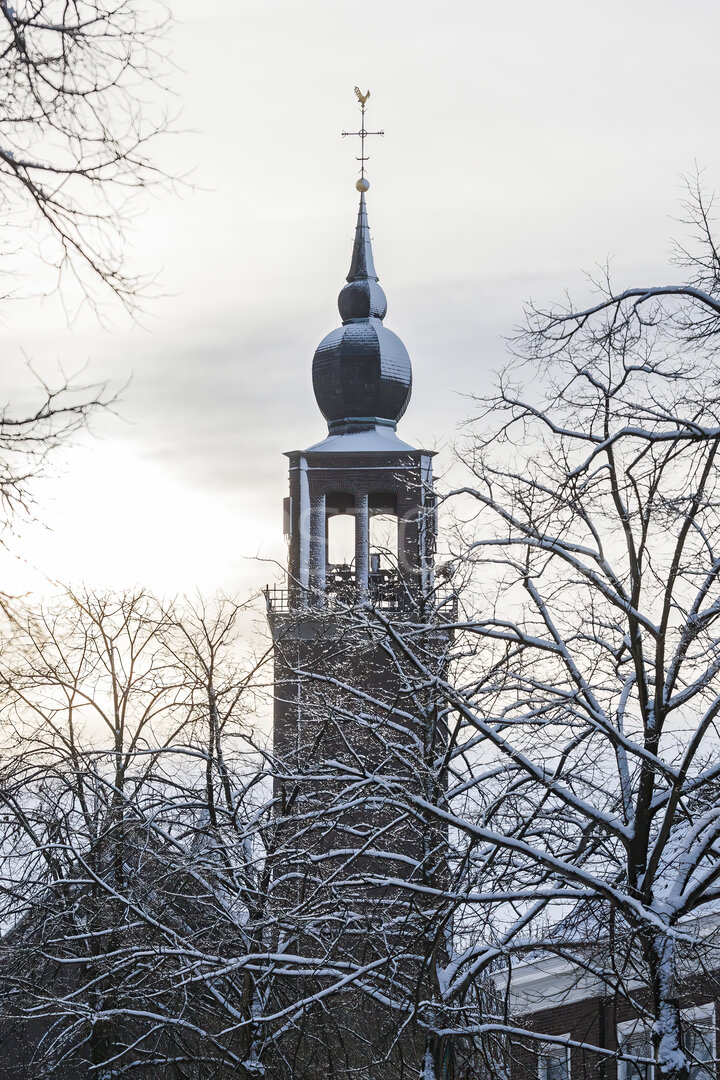 Sneeuwbedekte kerktoren tussen kale bomen bij zonsondergang