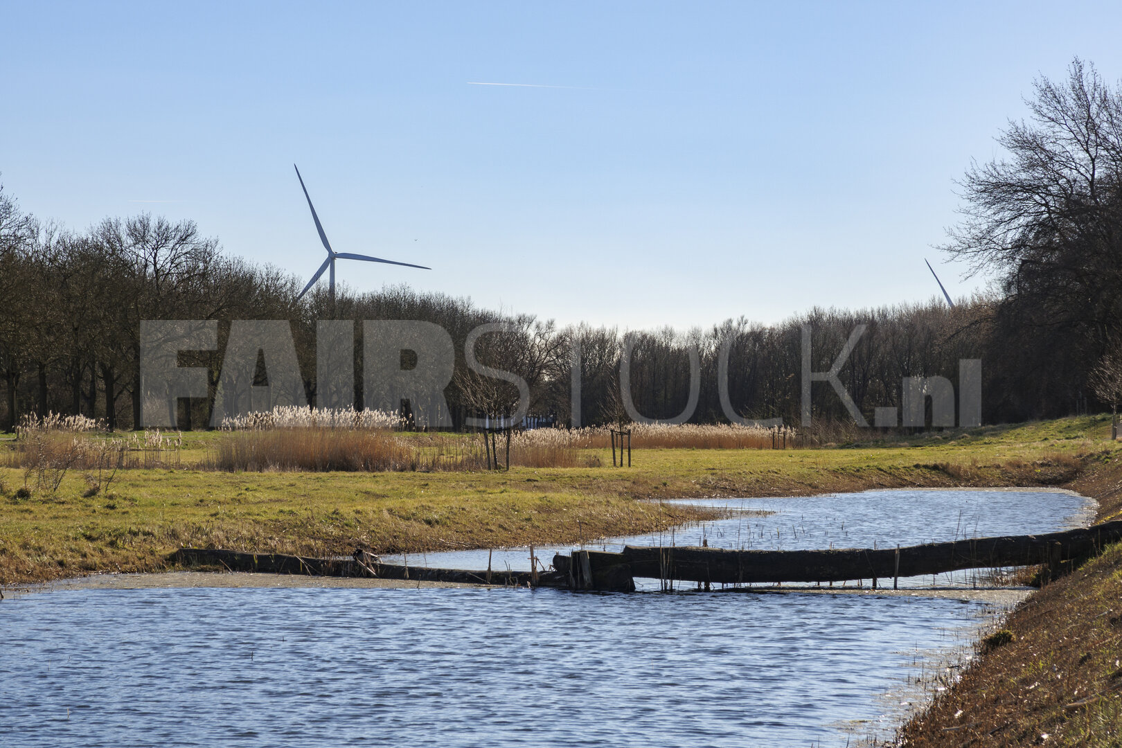 Wind turbines stand tall beside a tranquil river surrounded by t