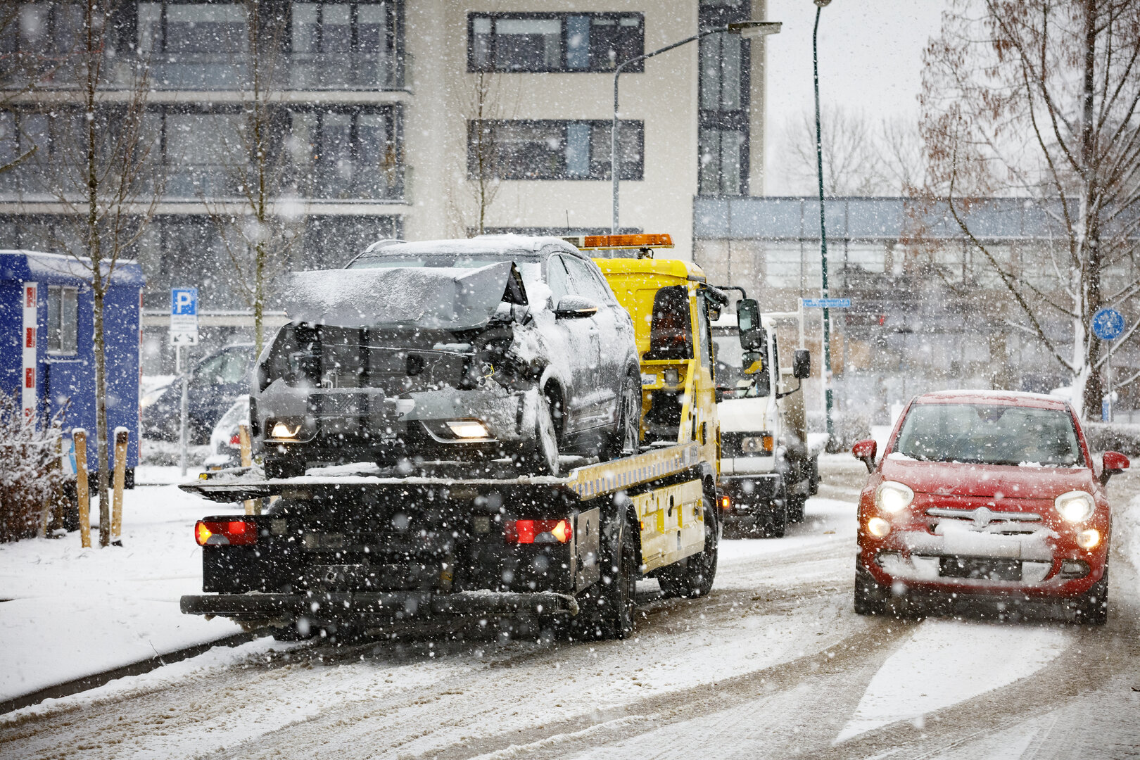 Takelwagen vervoert beschadigde auto in besneeuwde stad