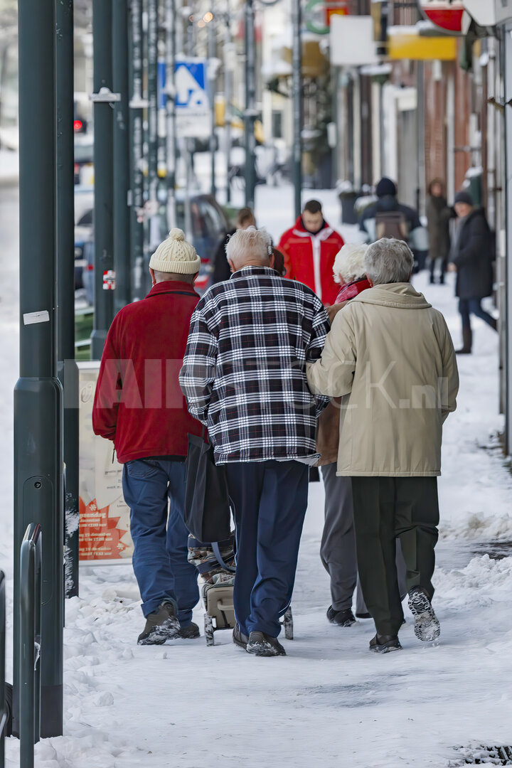 Oudere stellen wandelen samen door besneeuwde straat