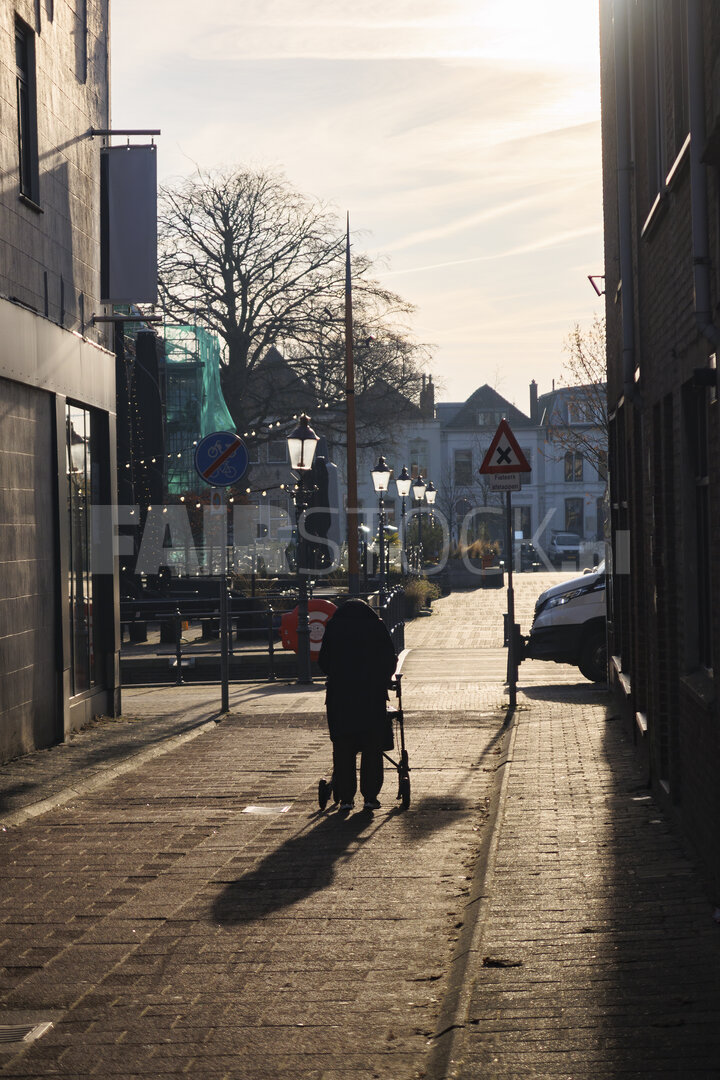 Oude vrouw met rollator wandelen in rustige stadstraat tijdens avond