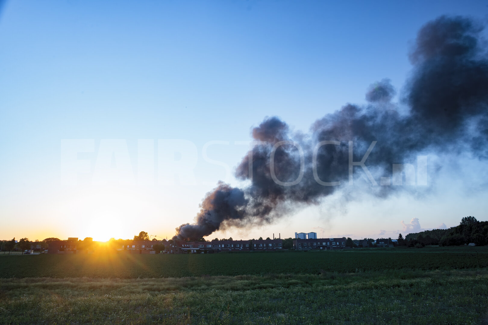 Rook boven Nederlandse stad bij zonsondergang